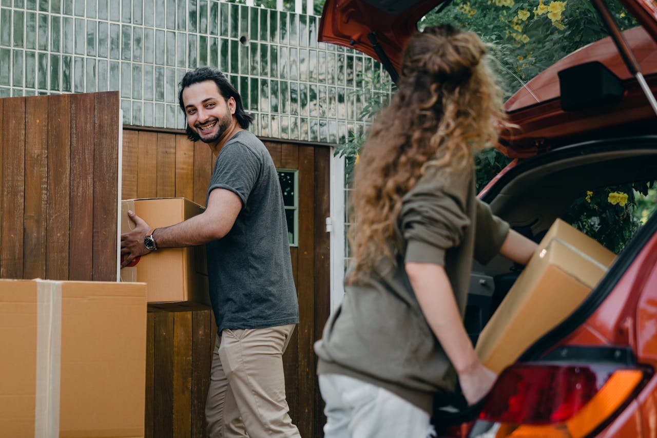 services-img Cheerful modern male and female in comfortable casual clothes unpacking car trunk in green garden of new house while moving in together