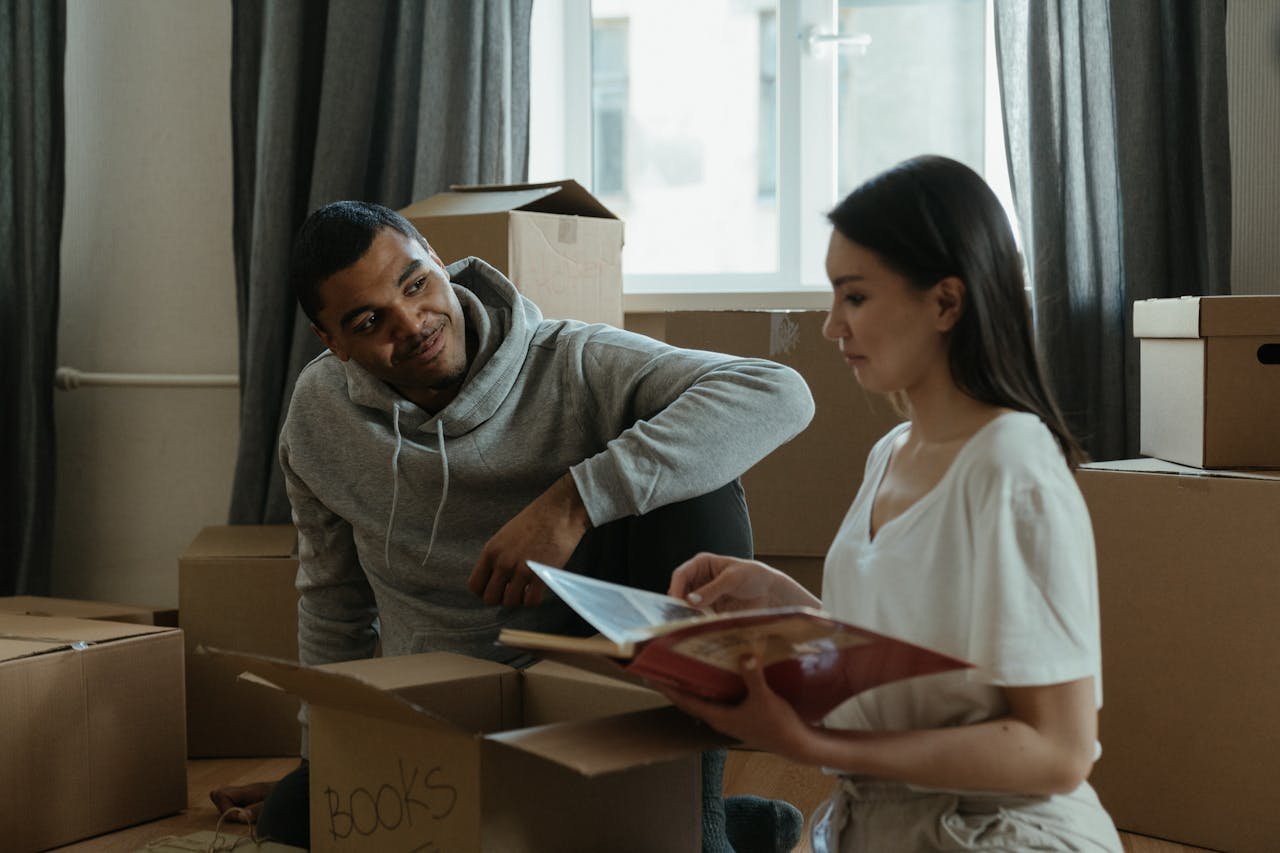 contact-img A couple exploring their new home while unpacking boxes and looking at a photo album.